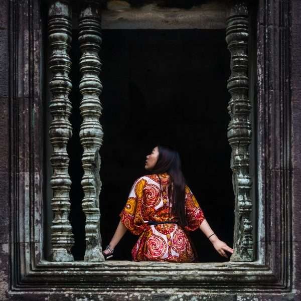 This is a photograph of a woman seated at a window of a Krong Siem Reap Temple and it's a photograph taken by Jacob Sammut
