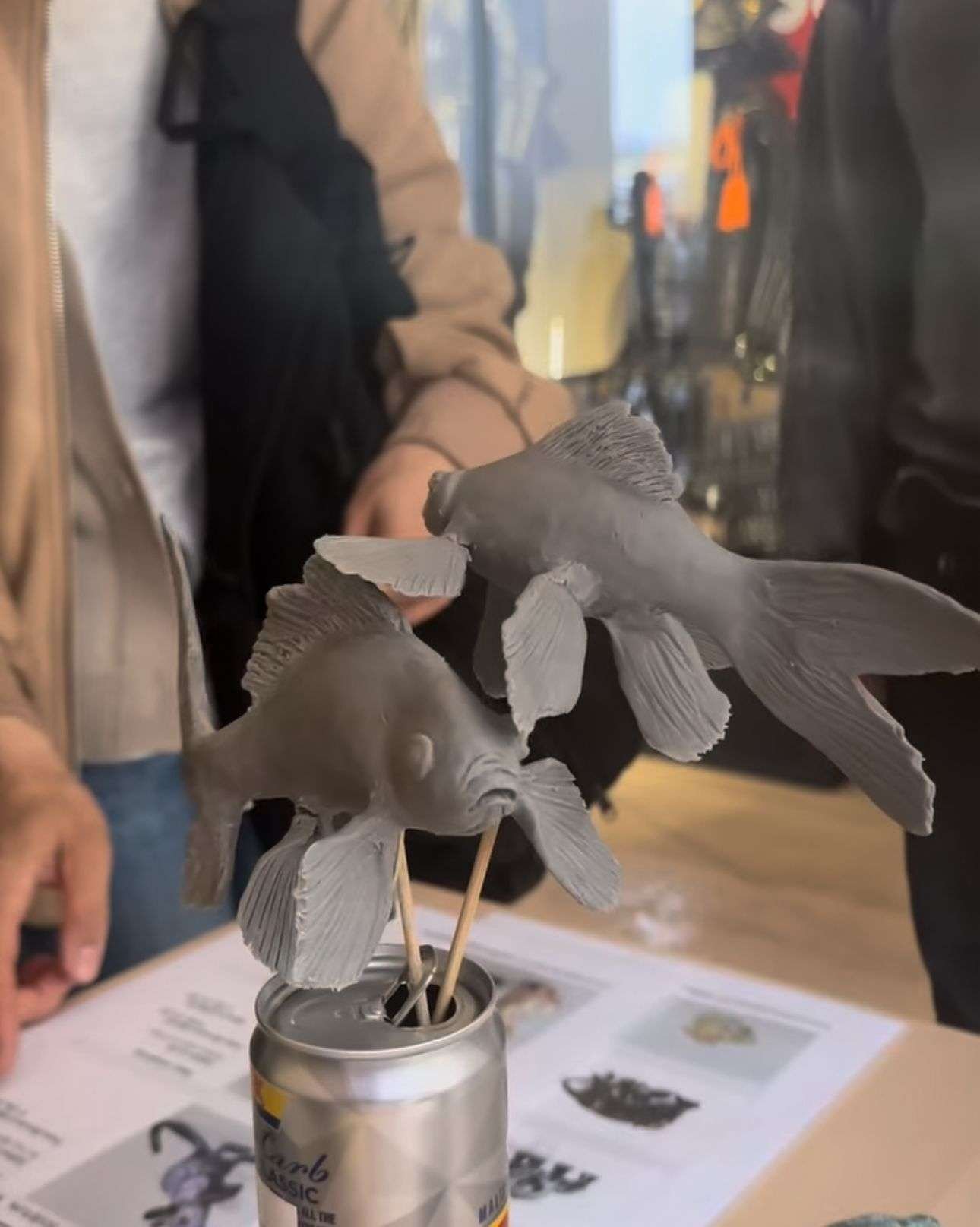 This photo depicts some fish clay sculptures that Amelia Saint George was working on whilst at the Malta pavilion at the Japan expo last week. The Koi fish are attached to sticks and placed in a Cisk lager can whilst visitors look at the work she presents.